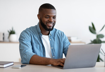 Remote Work. Handsome Black Freelancer Guy Working On Laptop At Home Office, Sitting At Desk With Computer, Smiling African American Man Looking At Device Screen, Enjoying Freelance Job, Copy Space