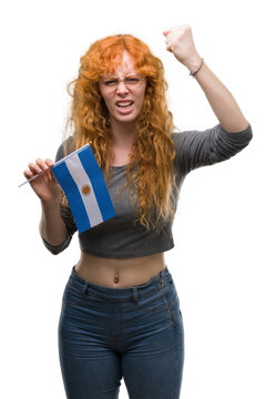 Young redhead woman holding flag of Argentina annoyed and frustrated shouting with anger, crazy and yelling with raised hand, anger concept