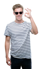 Young handsome blond man wearing sunglasess doing ok sign with fingers, excellent symbol