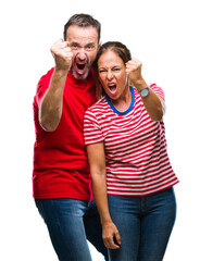 Middle age hispanic couple in love over isolated background angry and mad raising fist frustrated and furious while shouting with anger. Rage and aggressive concept.