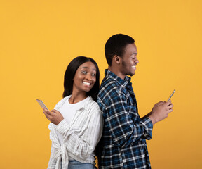 Blogs, social media, unusual message and interesting event. Cheerful young african american lady look over shoulder in smartphone of smiling husband, isolated on yellow background, studio shot
