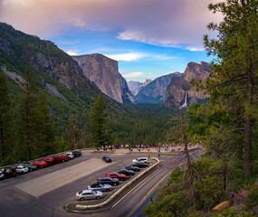 A scenic view from Tunnel View in Yosemite National Park, California, featuring El Capitan, Bridalveil Fall, and a parking area with tourists enjoying the iconic landscape.