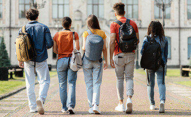 Obraz premium Group of five students with backpacks walking at university campus together, rear view of multiethnic young people going to classes, diverse college friends spending time outdoors after lessons