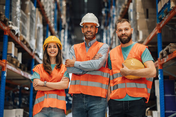 Warehouse workers posing with arms crossed wearing reflective vests and hard hats