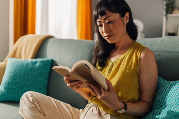 Concentrated asian woman reading a book on a sofa