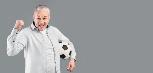 Mature Football Player. Excited cheering mature man posing with soccer ball on gray studio wall with winner gesture