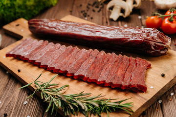 Sliced gourmet smoked salami on a wooden board with herbs, perfect for charcuterie boards and snacks