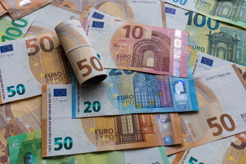 Mixed Euro banknotes with a rolled fifty Euro bill. A collection of colorful Euro banknotes, including denominations of 50, 20, and 10 Euros.