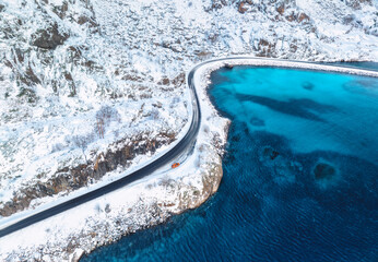Aerial view of curved snowy road to the island and blue sea at sunset. Highway in snow and azure...