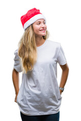 Young beautiful blonde woman wearing christmas hat over isolated background looking away to side with smile on face, natural expression. Laughing confident.