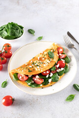 Stuffed omelette with tomatoes, cheese and spinach on a white background. 