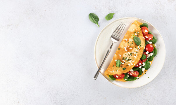 Stuffed omelette with tomatoes, cheese and spinach on a white background. Top view.
