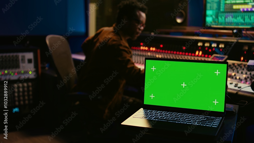 Poster Skilled audio technician processing and mixing sounds next to mockup display on laptop, using variety on knobs, buttons and sliders to edit audio recordings and produce new music. Camera B.