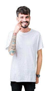 Young handsome man wearing white t-shirt over isolated background Pointing to the eye watching you gesture, suspicious expression