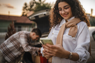 boyfriend pack shopping bags into trunk while girlfriend use cellphone