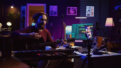 Guitarist instructor teaching guitar lessons online on internet, recording video on smartphone as a tutorial. Singer explaining acoustic instrument techniques, gives musical assistance. Camera B.