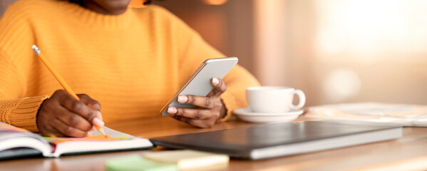 Cropped photo of black woman taking notes and using smartphone