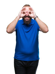 Young caucasian hipster man wearing blue shirt over isolated background doing ok gesture like binoculars sticking tongue out, eyes looking through fingers. Crazy expression.