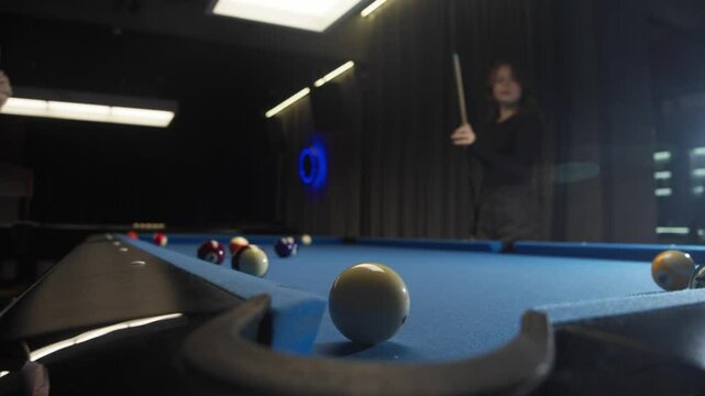 A beautiful young red-haired woman drives a red American pool ball into the pocket of a blue billiard table with a precise blow