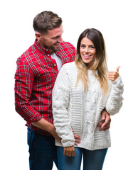 Young couple in love wearing winter sweater over isolated background smiling with happy face looking and pointing to the side with thumb up.