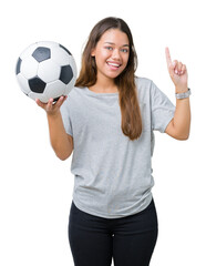 Young beautiful brunette woman holding soccer football ball over isolated background surprised with an idea or question pointing finger with happy face, number one