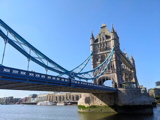 Obraz premium London, UK - 2023.07.02: Side view of Tower Bridge with Queen Elizabeth II Silver Jubilee repainting of blue and white over River Thames under a clear blue sky with sunlight coming from the left
