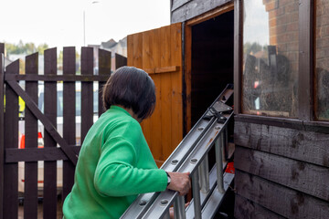Senior woman storing aluminum metal ladder in home backyard garden storage shed or hut © Tosh Lubek
