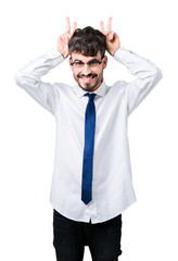 Young handsome business man wearing glasses over isolated background Posing funny and crazy with fingers on head as bunny ears, smiling cheerful