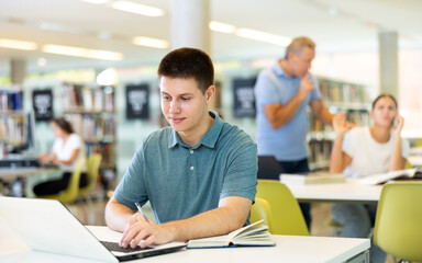 Fototapeta premium Young male student studying with a laptop in the library