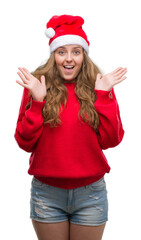 Young blonde woman wearing santa claus hat very happy and excited, winner expression celebrating victory screaming with big smile and raised hands