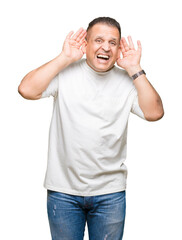 Fototapeta premium Middle age arab man wearig white t-shirt over isolated background Trying to hear both hands on ear gesture, curious for gossip. Hearing problem, deaf