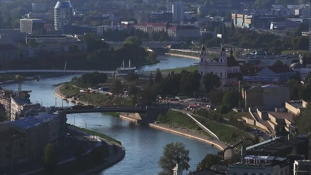 Vilnius urban landscape features modern and historical architecture, the Neris River, and St. Raphael Church, with solar panels indicating sustainability.