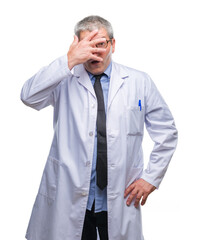 Handsome senior doctor, scientist professional man wearing white coat over isolated background peeking in shock covering face and eyes with hand, looking through fingers with embarrassed expression.