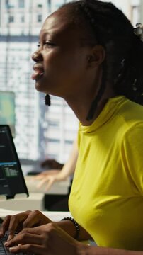 Vertical video Tired african american programmer having strained eyesight from overworking in office. Close up of woman at work removing eyeglasses to rub eyes, looking at PC screen for too long