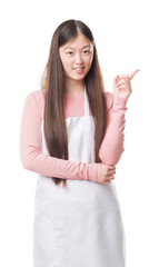 Young Chinese shop owner woman over isolated background wearing white apron very happy pointing with hand and finger to the side