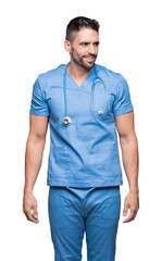 Handsome young doctor surgeon man over isolated background looking away to side with smile on face, natural expression. Laughing confident.