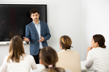 Fototapeta premium Young male tutor teaching students in college classroom
