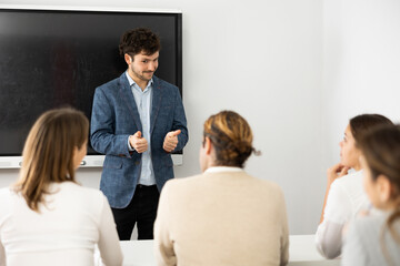 Fototapeta premium Young male teacher near interactive board, gesturing with hand while consecrating topic of lesson for adults in classroom