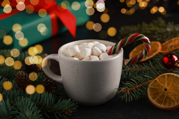 Tasty hot cocoa drink with marshmallows, candy cane in cup and Christmas decor on table, closeup