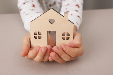 Adoption. Little girl with house figure at beige table, closeup