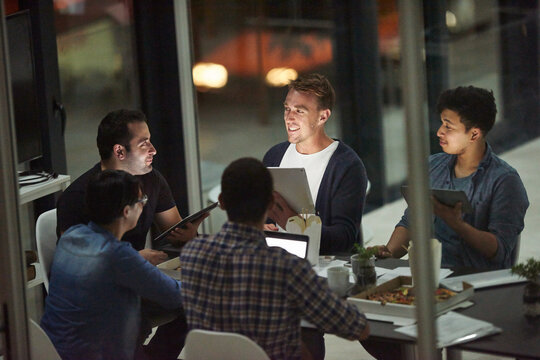 Business people, discussion and planning with tablet at night for brainstorming, design or web strategy in office. Young, group or creative employees working late on technology for ideas at workplace