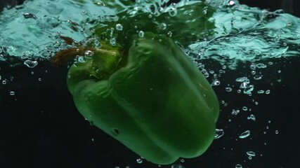 Close up of a fresh green bell pepper floating in water. The pepper is round with a green stem at the top. Macro of green bell pepper dropping in to water and splashing with black background. Pabulum. - Powered by Adobe