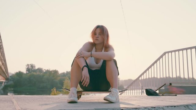Teen Girl on Skateboard at Sunset: Redhead Skater Posing by River | Cool Urban Scene with Bridge | Slow Motion of Confident Youth