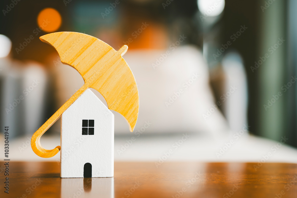 Wall mural Model of umbrella with house on wooden table concept of the system of insurance savings and Housing insurance against impending loss and fire, building fire insurance concepts.