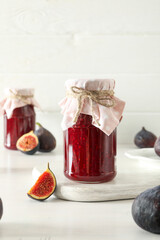 Figs and jars of jam on light background