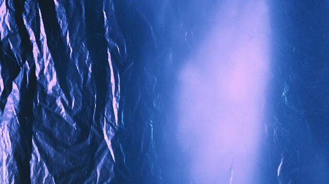 Crumpled foil. Wrinkled texture. Defocused shiny blue color distressed polyethylene film with lens flare effect swaying motion abstract background.