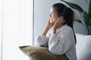 Asian woman sits on sofa listening to music in living room