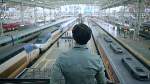 Rear View of Man Moving Down On Escalator At Seoul KTX Train Station Overlooking Many Railway Speed Trains Arriving and Waiting For Departure - High rise slow motion