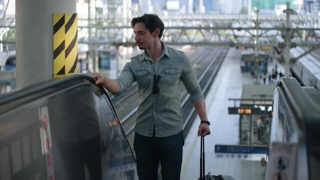 Happy Tourist Man Moving Up On Escalator At Seoul KTX Train Station Overlooking Many Railway Tracks in Background