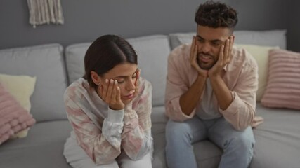 Man and woman sitting on a couch at home looking sad in a living room together
